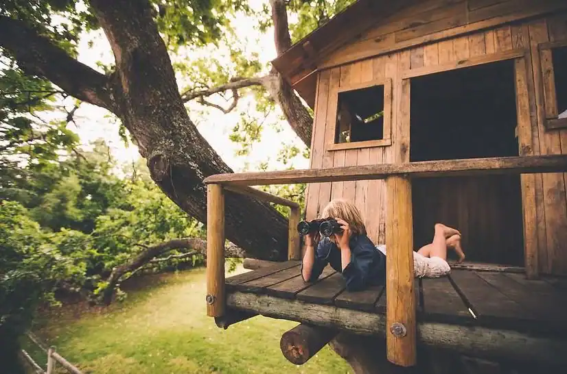 Enfant dans une cabane en bois, jumelles à la main — explorer le monde à son rythme