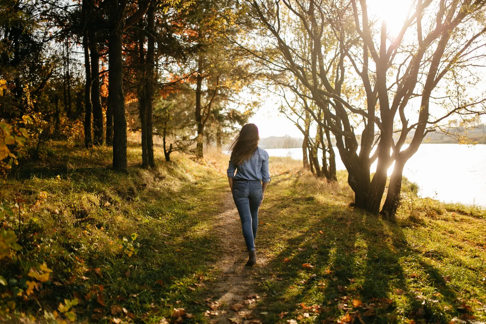 Femme marchant sur un sentier au bord d'un lac, dans la lumière dorée d'automne